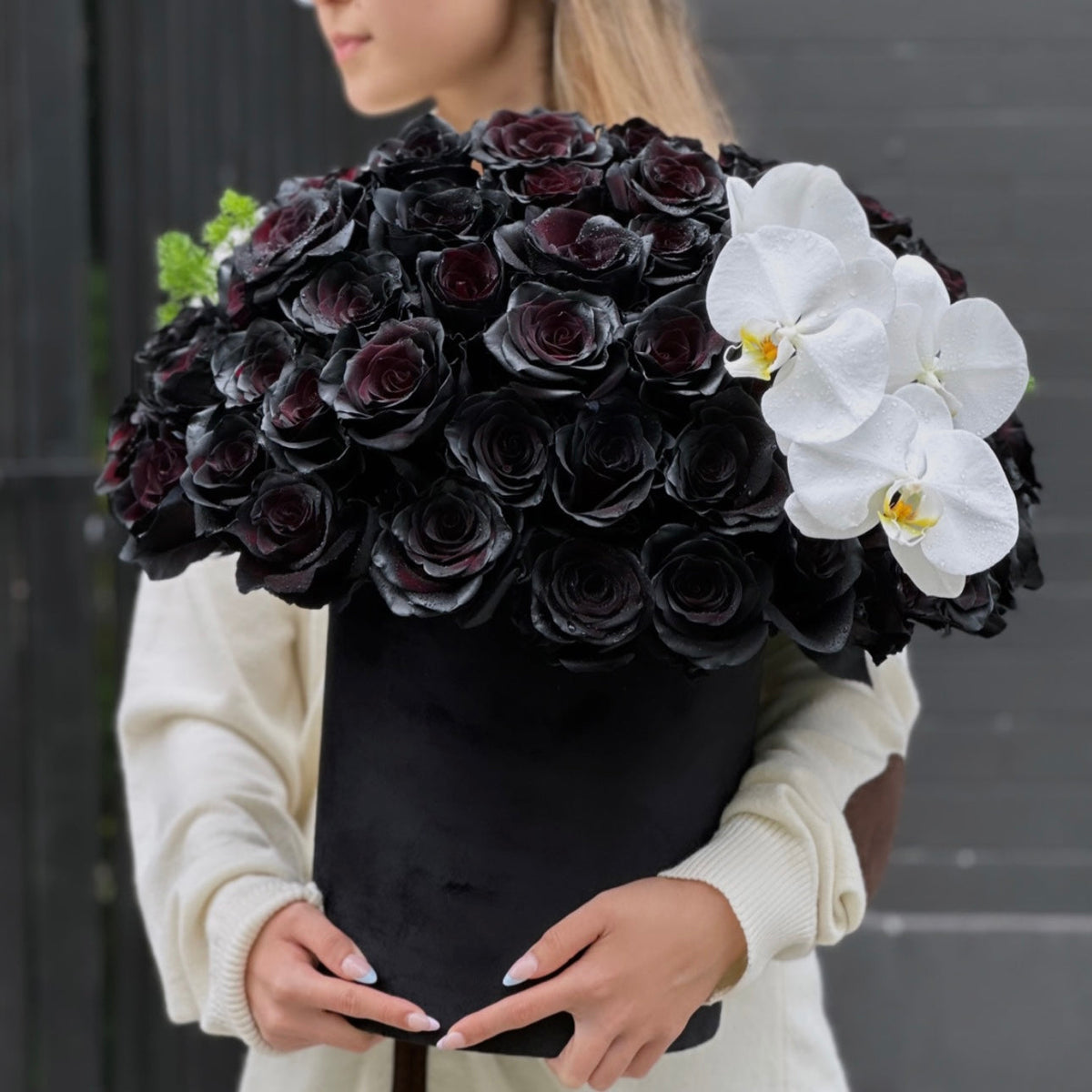 Black roses and white orchids in a精致 keepsake box, surrounded by lush greenery – a bold and elegant floral arrangement from Pink Clover LA.