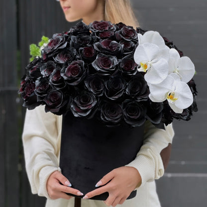 Black roses and white orchids in a精致 keepsake box, surrounded by lush greenery – a bold and elegant floral arrangement from Pink Clover LA.