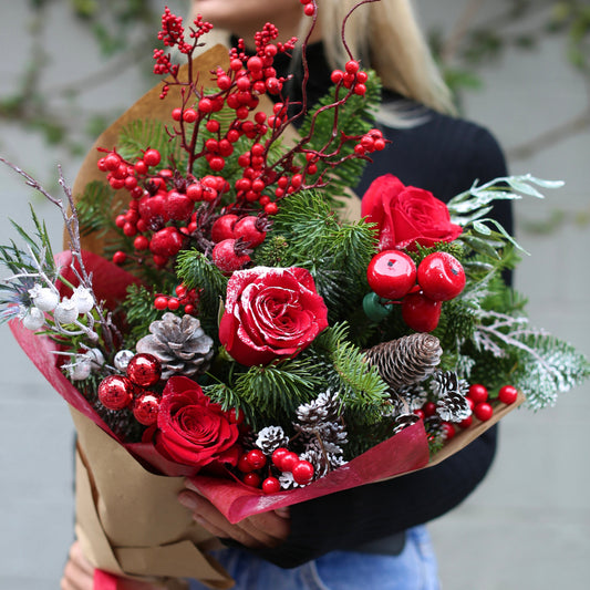 Festive Christmas bouquet featuring red roses, pine branches, and pinecones arranged in a decorative style with a holiday toy accent
