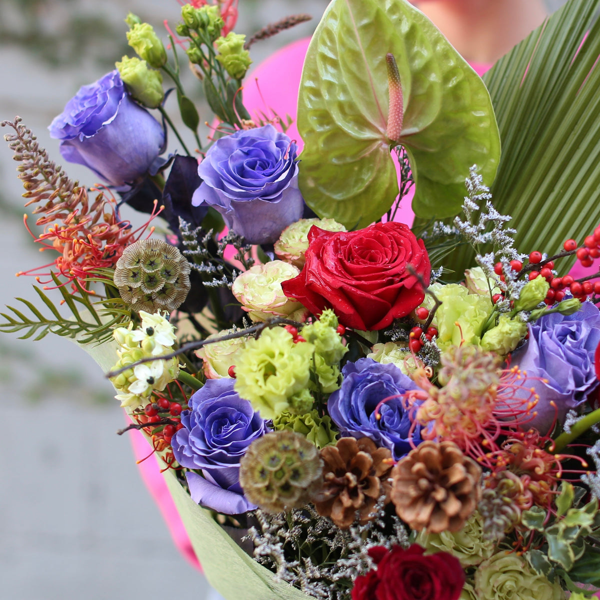 Vibrant red rose bouquet accented with natural holiday elements, beautifully styled for Christmas gifting