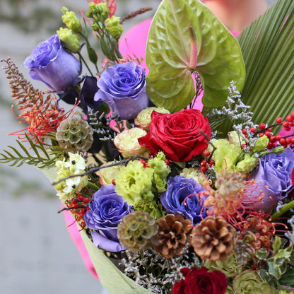 Vibrant red rose bouquet accented with natural holiday elements, beautifully styled for Christmas gifting