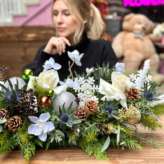 Elegant white Christmas floral arrangement featuring roses, carnations and festive accents in a snowy color palette