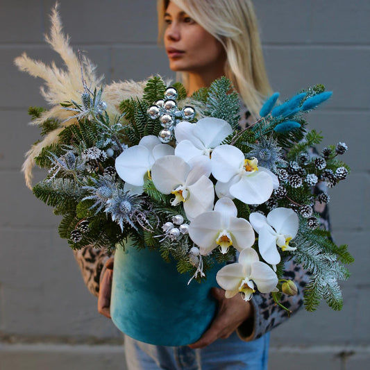 Festive floral design with blue and white tones, showcasing fresh pine and orchids for a luxurious holiday look