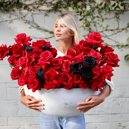 Dramatic Halloween bouquet featuring red roses, black accents, and raven decor in a premium stone vessel – ideal for luxury floral gifting