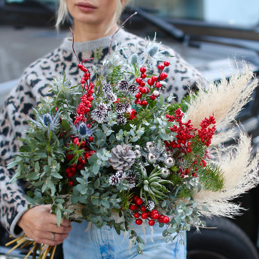 Vibrant Christmas bouquet with red berries, pinecones and frosted foliage, styled for festive holiday gifting