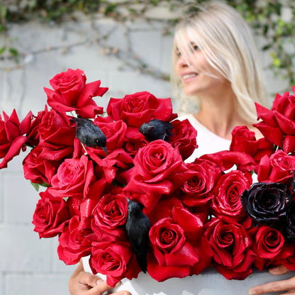 Elegant red and black rose arrangement styled with dark accents and decorative ravens, perfect for Halloween celebrations and premium delivery