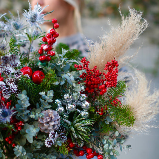 Festive floral arrangement showcasing silvery pinecones, blue thistle and lush greenery in a celebratory winter-inspired design