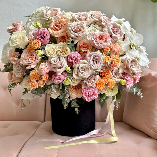 Compact pastel bouquet with peonies, spray roses, and lush greenery wrapped in kraft paper and satin ribbon – Candy Box by Pink Clover LA.
