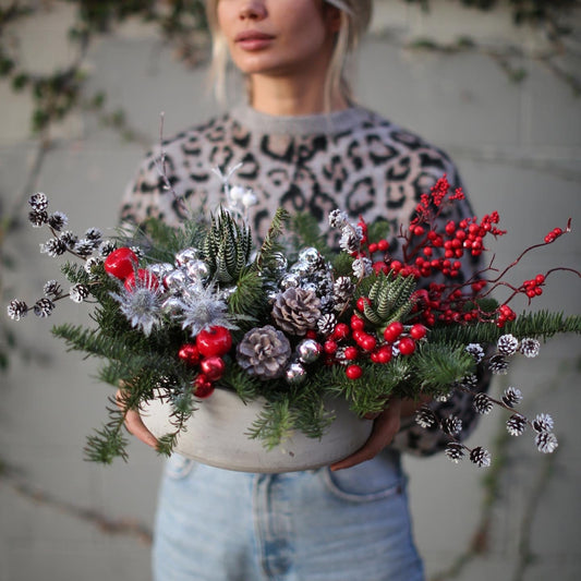 Festive floral arrangement showcasing silvery pinecones, blue thistle and lush greenery in a celebratory winter-inspired design