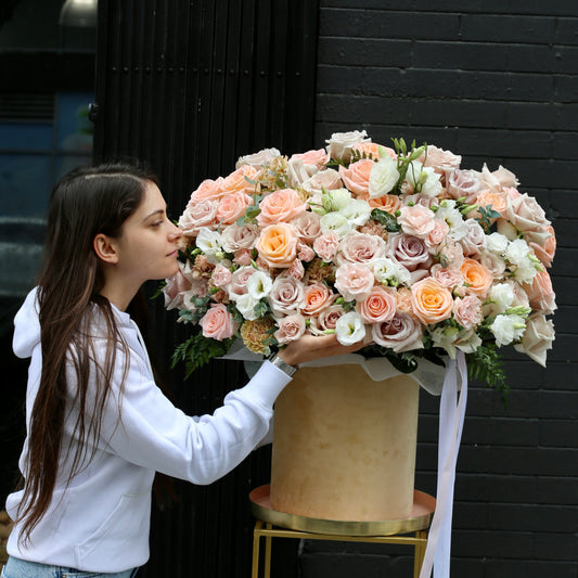 Hand-tied bouquet of peach and cream roses with greenery wrapped in kraft paper and satin ribbon – Peach Paradise by Pink Clover LA.